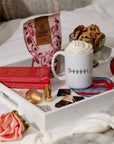 Elements rose hot chocolate mix on a breakfast tray with a whipped cream mug and cookies