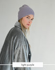 A woman wearing a light purple ribbed knit beanie and a gray plush jacket, shown in profile against a plain light gray background. A label at the bottom reads 'light purple'.