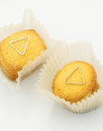 Yellow cookies in paper liners with two 8.6.4 triangle ear cuffs, one brass and one silver, on a white background.