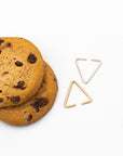 Two 8.64 triangle ear cuffs: one brass, one silver, on a white table next to chocolate chip cookies.