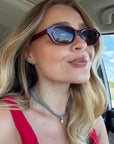 Woman in dark red sunglasses and a red top wearing small turquoise stud earrings, selfie in a car