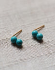 Pair of turquoise double bead stud earrings with gold-filled posts on gray linen