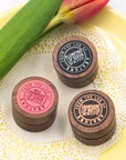 Three wooden lip product containers from small business, Abature, with labels on a decorative plate with tulips.