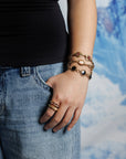 Close up of person's arm wearing 3 vintage bracelets including cameos, onyx stones and pink glass adn two, gold rings with handpainted glass centers.