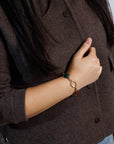 Close up of woman's arm in a brown sweater wearing an antique scarab bracelet featuring rare clear quartz, carnelian and green chalcedony.