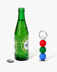 Red, green blue bottle opener next to a green glass bottle.