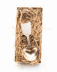 Metal coffee scoop with heart and arrow design in a box of straw on a white background.