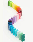 Rainbow gradient wooden dominoes standing in an S-shaped line on white