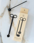 Matte black candle wick snipper and snuffer next to their cream Botanica box
