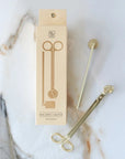 Matte brass candle wick snipper and snuffer next to their cream Botanica box