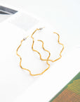 Gold wavy hoop earrings on an open book with a white background