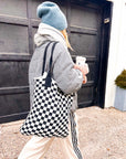 Woman in a puffer jacket walking with the Casupo black and white checkered woven tote