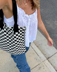 Woman walking while wearing a woven black and white checkered tote bag from Casupo paired with a white top and a pair of jeans.