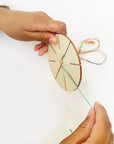 Hands braiding colorful thread on a wooden friendship bracelet disc