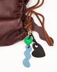 Close-up of Dyad chocolate brown leather bag with colorful deadstock-leather charms in blue and black.