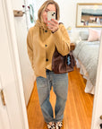 Woman wearing Dyad chocolate brown leather bag crossbody with jeans and tan jacket.