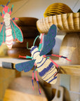 Screen-printed paper bee from the insect garland hanging beside wooden kitchen shelves