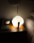 Gingko origami book light glowing open in a fan shape on a dark nightstand