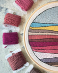 Close-up of the landscape embroidery's stitched bands of pink, mustard and blue