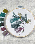 Finished Pine Boughs embroidery in teal, green and plum thread with floss bobbins
