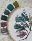 Pine Boughs embroidery in an 8-inch hoop beside wound green and plum floss