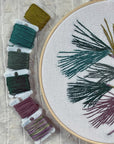 Kate Wyatt pine branch embroidery in progress beside bobbins of green and gray floss