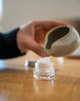 Hand pouring water from a ceramic dish onto the 'Rest Your Eyes' aromatherapy eye towel