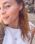 Woman wearing a gold necklace with a shell pendant outdoors