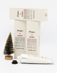 Opened tube of Mayron's Goods Hand Cream in front of 3 boxes next to a mini bristle Christmas tree.