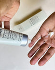 Close up of hands applying cream from a silver tube labeled 'Nourishing Creme' on a white background