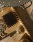 Cleaning tools including a kitchen soap, scrubber, brush, and sponge on a wooden surface.