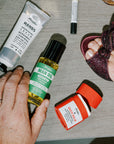 Man body care products including a tube of hand cream, bottle of man oil, and stick of ouch balm ointment on a table.