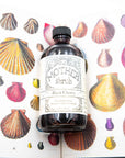 Bottle of Mother Shrub Black Cherry shrub on a background with colorful shells