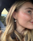 Woman in a car wearing a Daydreamer mini hoop earring with a white porcelain cloud charm
