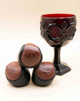 Three brown leather O-Sack hacky sacks stacked in front of a red glass goblet