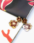 Floral gold and burgundy earrings on a colorful fabric background
