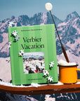 Verbier Vacation puzzle box with scattered pieces beside an orange mug in the mountains