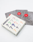 Riddles Vol. 1 card deck box resting on scattered riddle cards