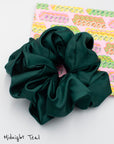 Midnight teal oversized satin scrunchie on decorative paper featuring pink, green and yellow vintage ribbon candies.