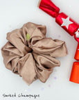 Giant, oversized satin scrunchie in smoked champagne color next to a festive red, Christmas cracker with a silver star.