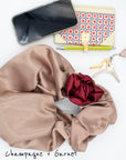 Champagne satin rosette clutch with garnet red hair tie, styled with wallet, keys, and lipstick.