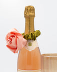Neck of a champagne bottle with satin rosette scrunchie on a white background