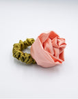 Satin peach colored rosette scrunchie with a cerulian green band, laying flat on a white background