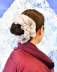 Close up of the back of a woman wearing burgundy puffer jacket with brown hair wearing a giant, oversized organza scrunchie in a cloud color over a bun.