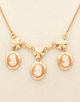 Close up of vintage 1940s gold-fill necklace with three carved shell cameos and gold floral accents on a 16-inch chain.