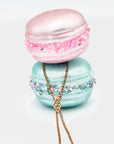 Two decorative macaron-shaped containers with an antique Victorian Chateleine necklace draped over them on a white background