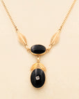 Close up of gold-fill necklace with two onyx stones in a drop-style design with gold-fill leaf accents and a central rhinestone.