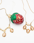 Two vintage gold-fill cameo necklaces featuring carved shell cameos and floral details, displayed with a strawberry holiday ornament
