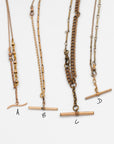 Close up of 4 necklaces labeled A, B, C, D made from Victorian-era men’s watch chains with antique T-bars and dog clips. Authentic 100+ year-old pieces made from sustainable vintage chains laying flat on a white background.