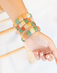 Close-up of a wrist wearing four stacked chicklet agate stone beaded bracelets in a mix of green, orange, yellow, and white stone beads.